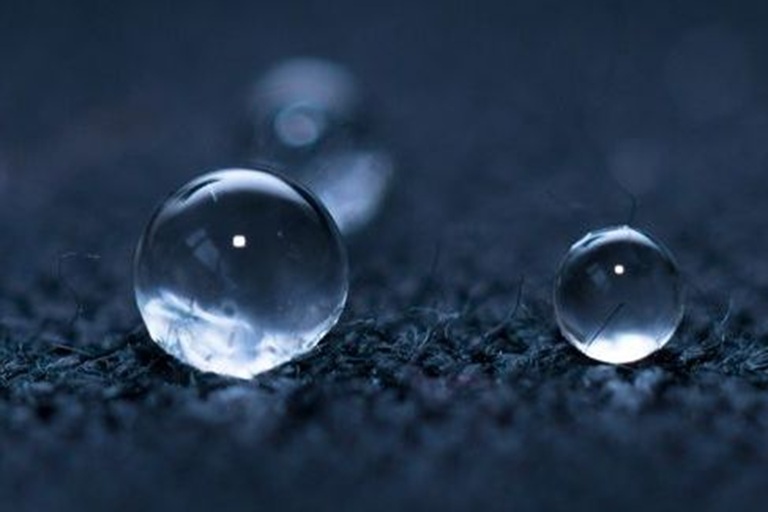 Water droplets with high contact angles on a textured hydrophobic surface, demonstrating low surface energy typical of amorphous fluoropolymers.